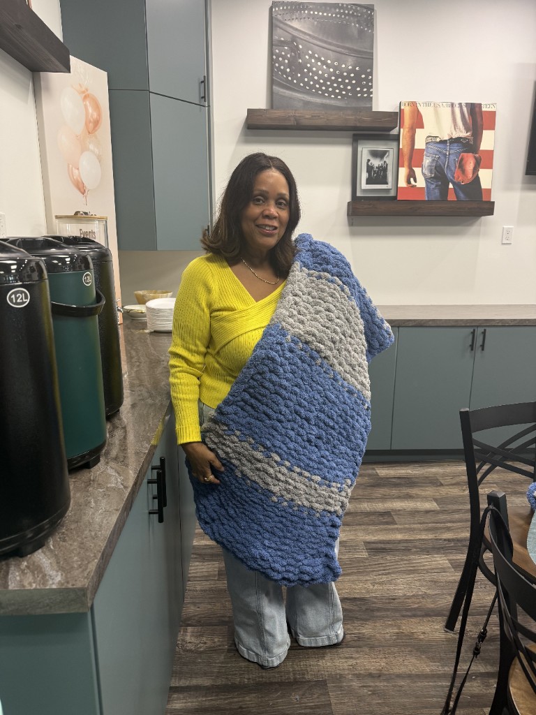Estelle holding a finished blue and grey chunky knit blanket