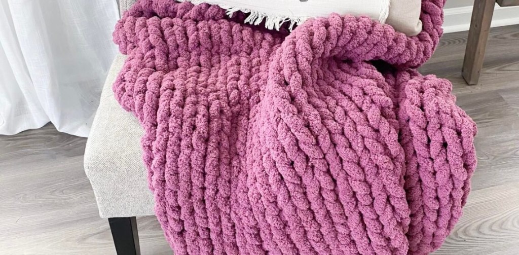 Mauve chunky knit blanket on a light gray upholstered chair