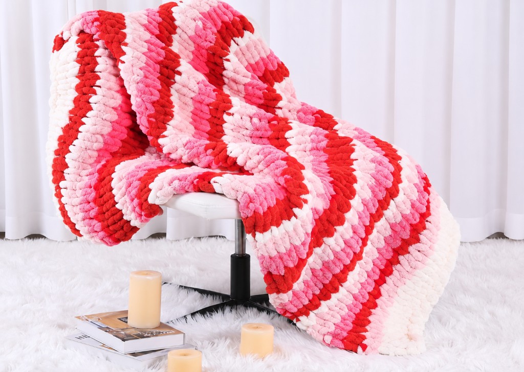 Red, pink, and cream chevron chunky knit blanket on a white chair