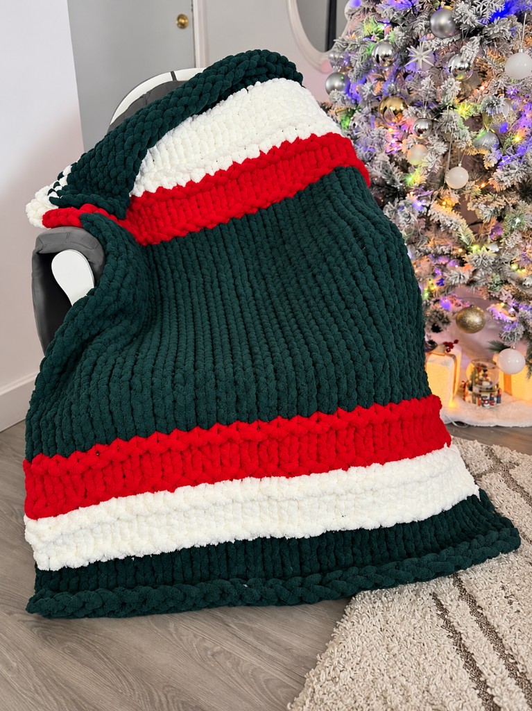 Forest green, red, and cream striped chunky knit blanket beside a Christmas tree