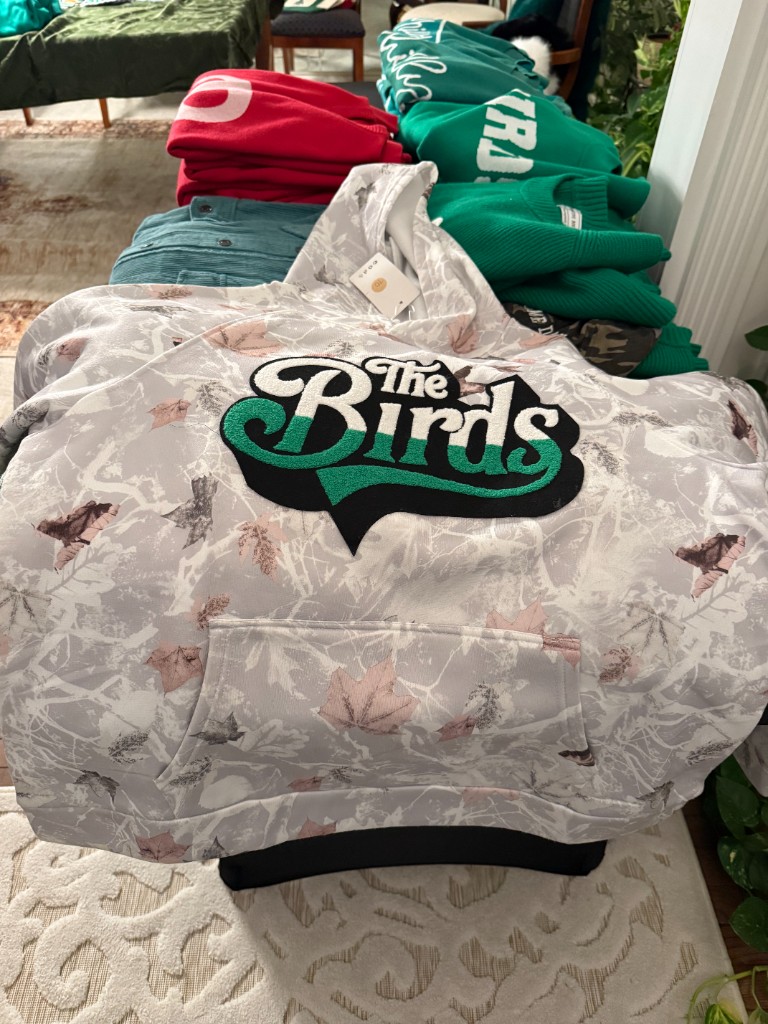 Camouflage hoodie with a large green and black The Birds patch