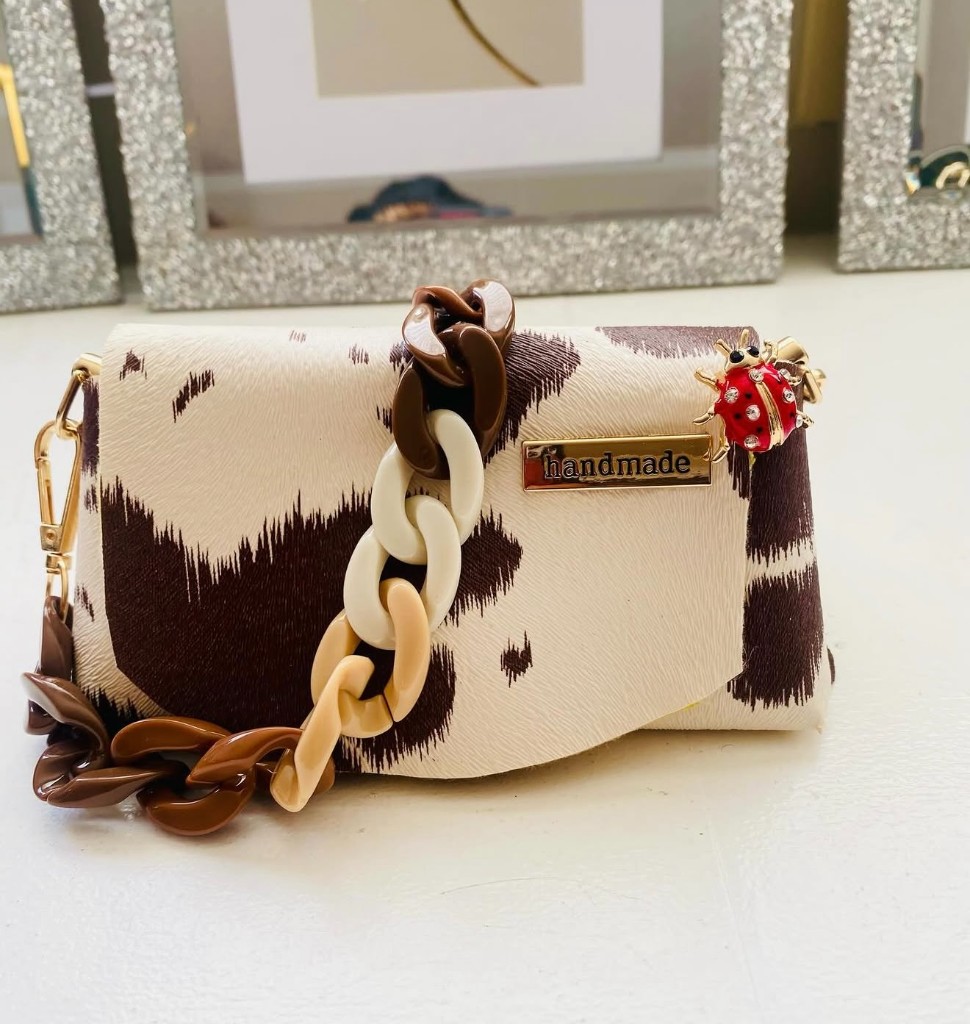 A cream and brown handmade purse with a chunky chain and ladybug charm