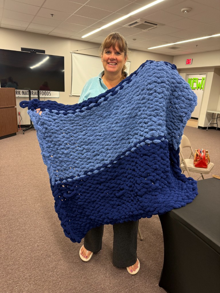 A smiling participant holding a large blue ombre chunky knit blanket