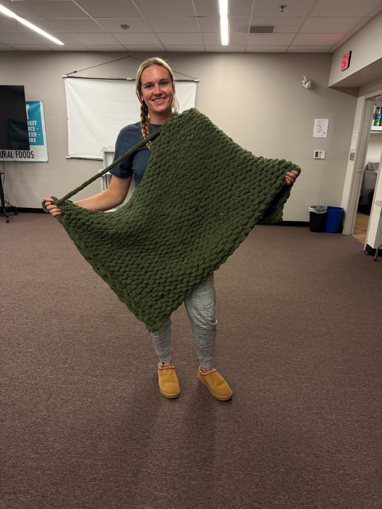 A smiling participant holding out an olive green chunky knit blanket