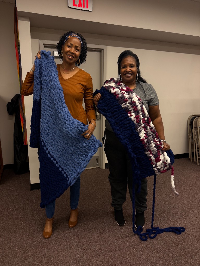 Two smiling participants showing blue and navy chunky knit blankets