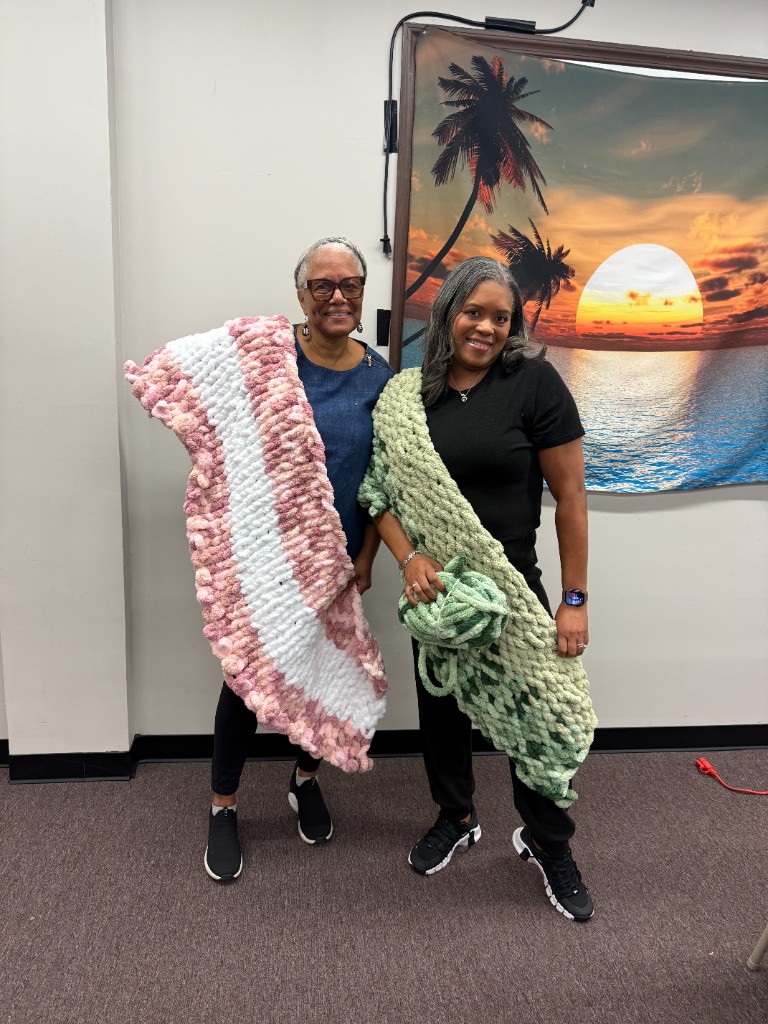 Two smiling participants holding a pink and white blanket and a sage green blanket