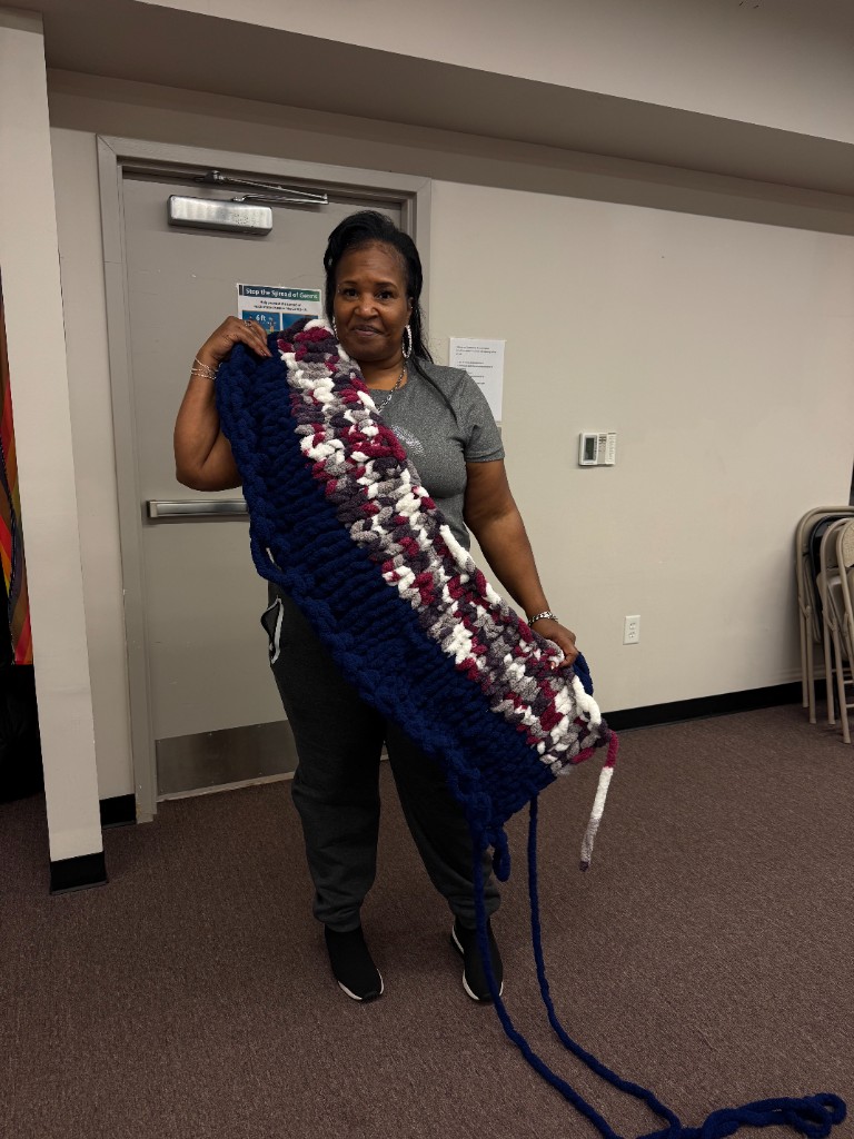 A participant holding a navy, burgundy, and cream chunky knit blanket